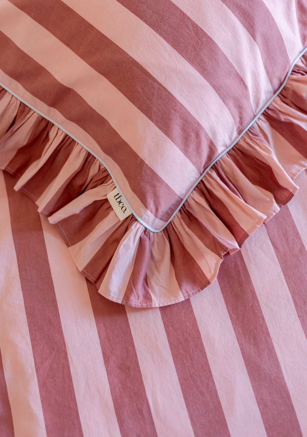 Pink and burgundy striped cotton pillowcases from TBCo featuring ruffled edges and classic wide stripes