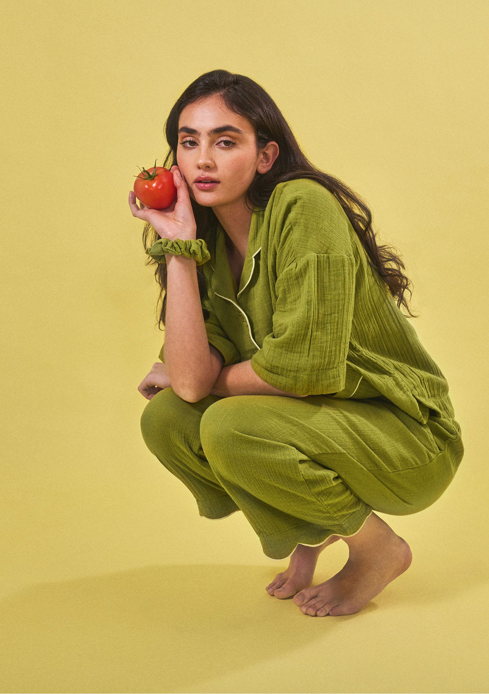 Portrait of a model crouching in TBCo Cropped Cotton Pyjamas in Green with yellow piping holding a tomato gallery 2
