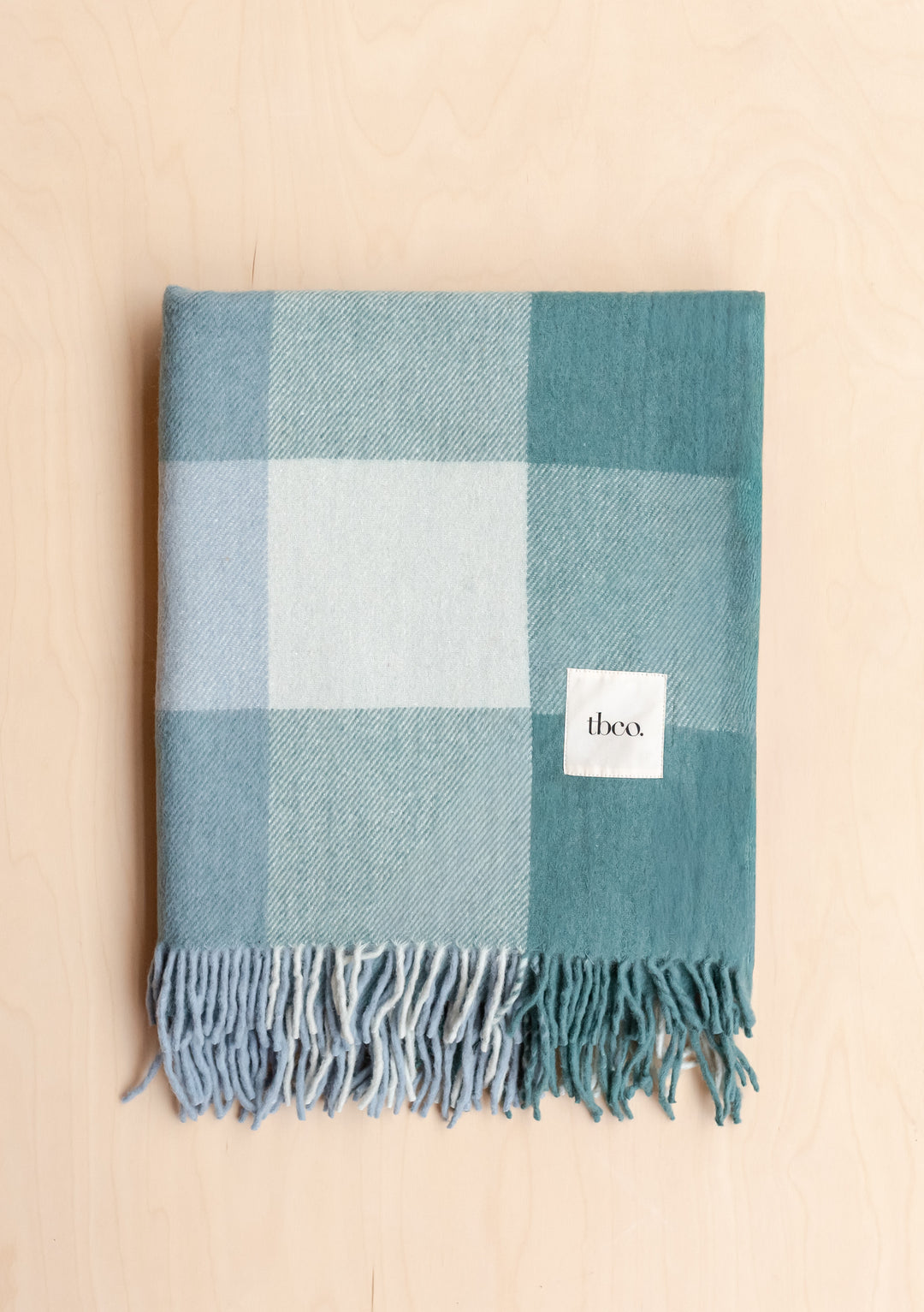 Folded Recycled Wool Blanket in Blue Bold Check by TBCo featuring soft fringed edges and large plaid pattern on pale wood