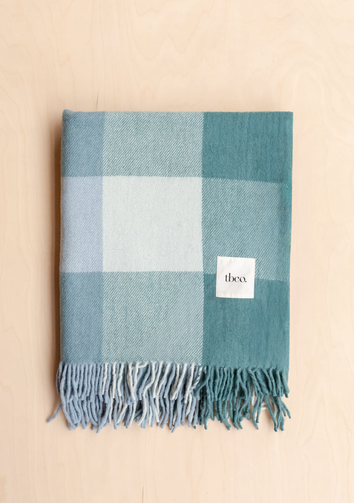 Folded Recycled Wool Blanket in Blue Bold Check by TBCo featuring soft fringed edges and large plaid pattern on pale wood