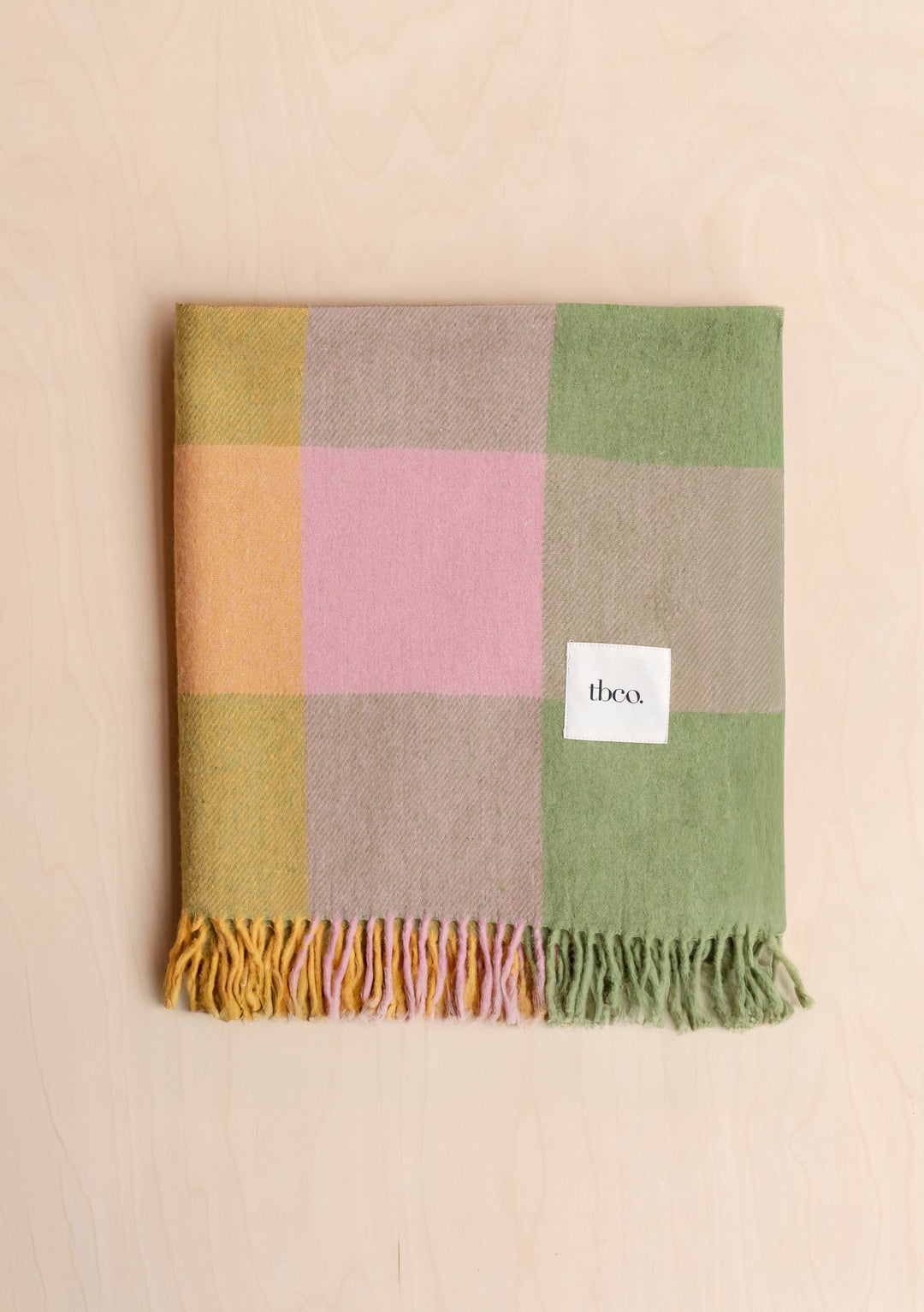 Folded TBCo Recycled Wool Blanket in Green Bold Check with soft wool fibres and colourful check pattern on pale wood background