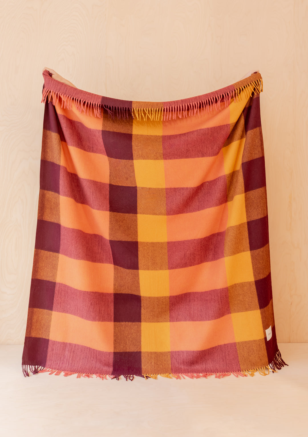 Recycled Wool Blanket in Ochre Bold Check by TBCo displayed hanging with fringed edges on pale wood background
