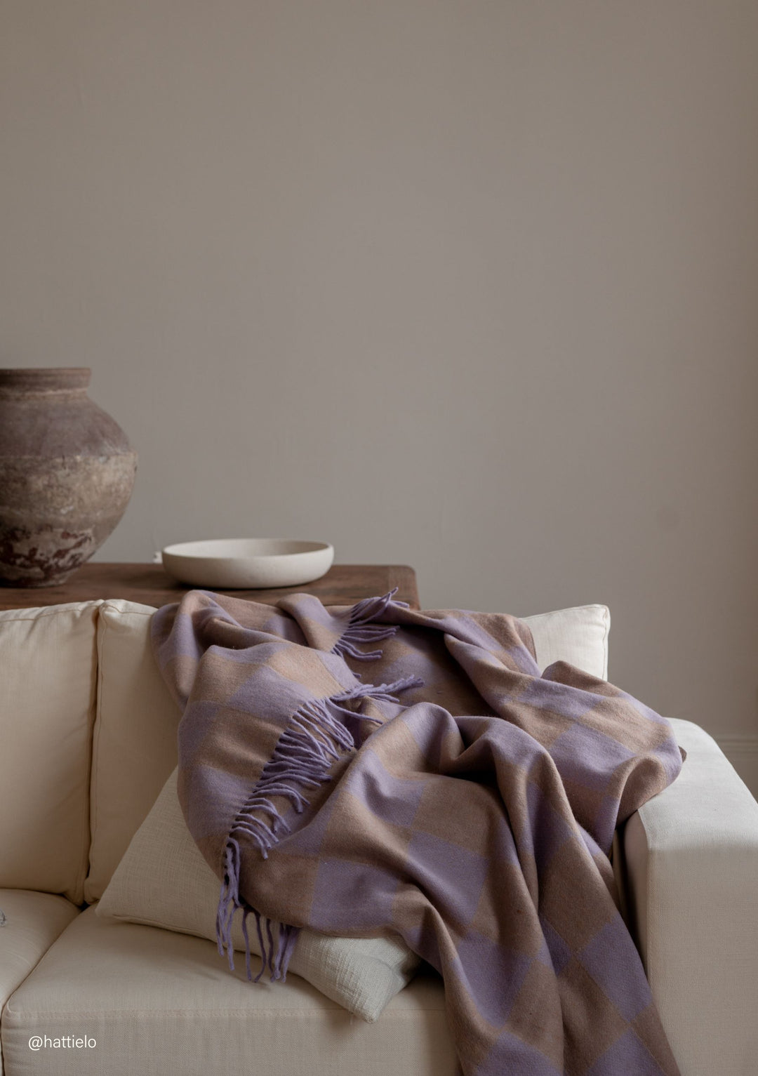 TBCo Recycled Wool Blanket in Lilac & Coffee Checkerboard casually draped over cream sofa with fringed edges visible