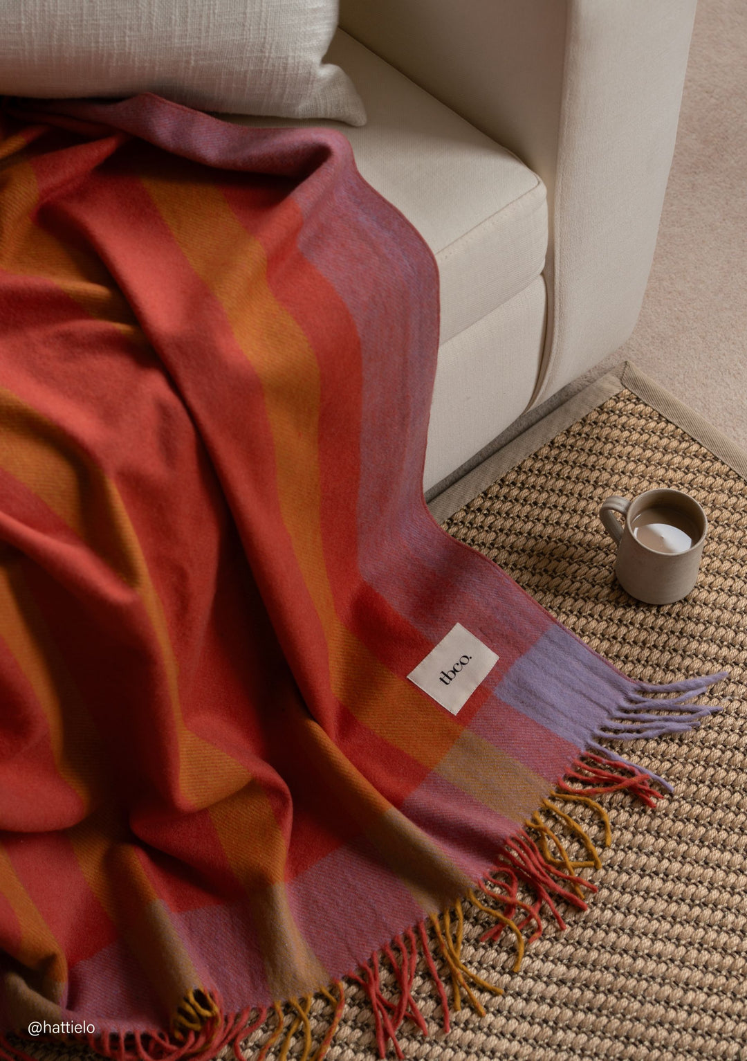 TBCo Recycled Wool Blanket in Orange Frame Stripe draped over sofa with fringed edges and woven rug beside a mug