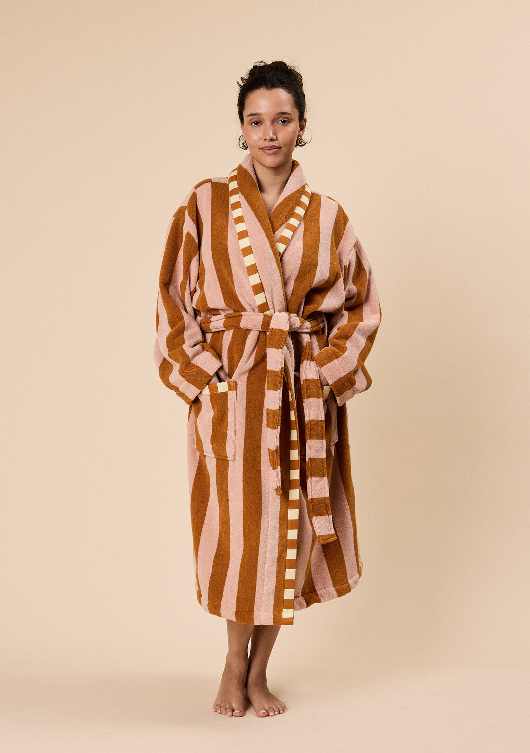 Woman wearing TBCo Terry Cotton Bath Robe in Honeycomb Stripe with warm brown and soft pink vertical stripes and belted waist