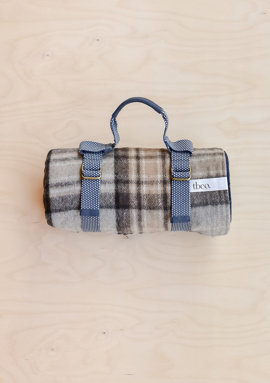 A TBCo recycled wool picnic blanket in Mackellar Tartan, rolled up and held in a recycled plastic TBCo picnic carrier.