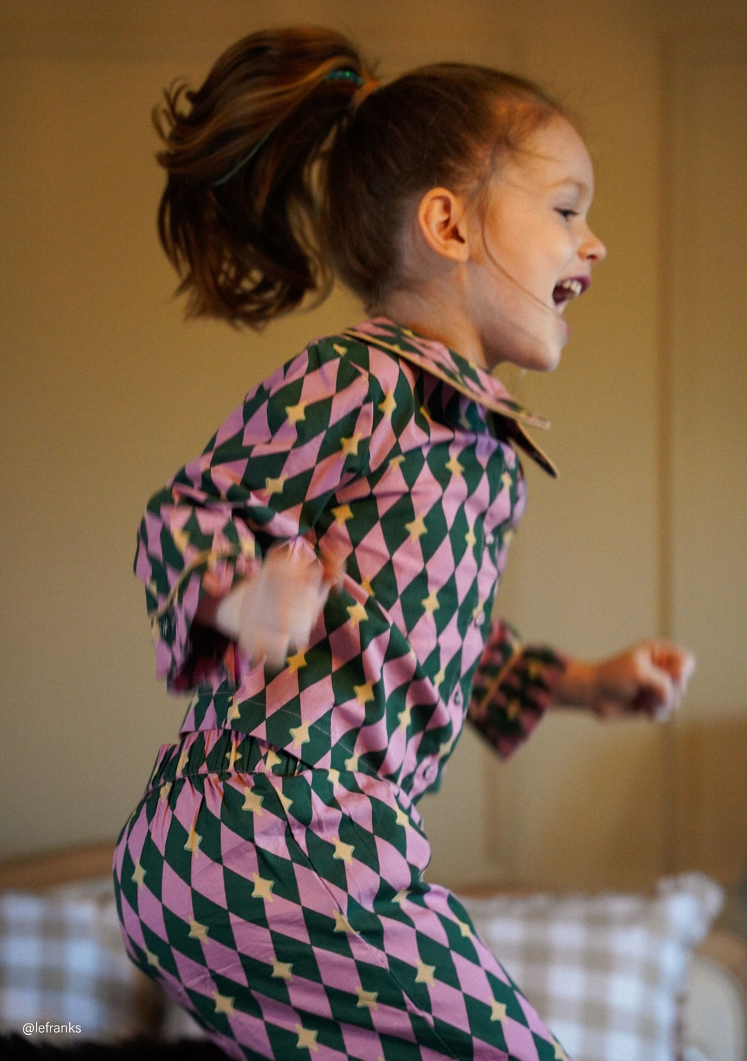 Child joyfully jumping indoors wearing TBCo Cotton Kids Pyjamas in Pink Harlequin with natural fibres, designed to make an impact