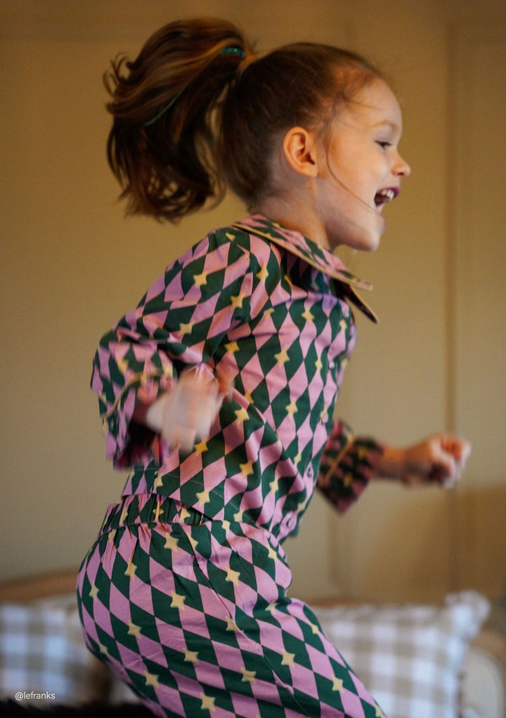 Child joyfully jumping indoors wearing TBCo Cotton Kids Pyjamas in Pink Harlequin with natural fibres, designed to make an impact