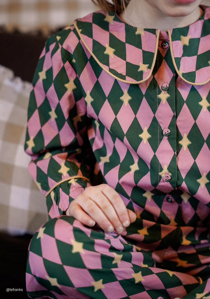 Child seated wearing TBCo Cotton Kids Pyjamas in Pink Harlequin featuring natural fibres and vintage-inspired collar designed to make an impact