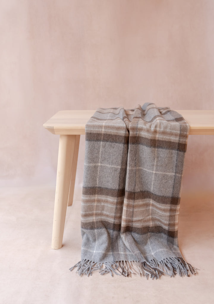 Cashmere Small Blanket in Mackellar Tartan by TBCo draped over a light wooden bench with fringe detailing