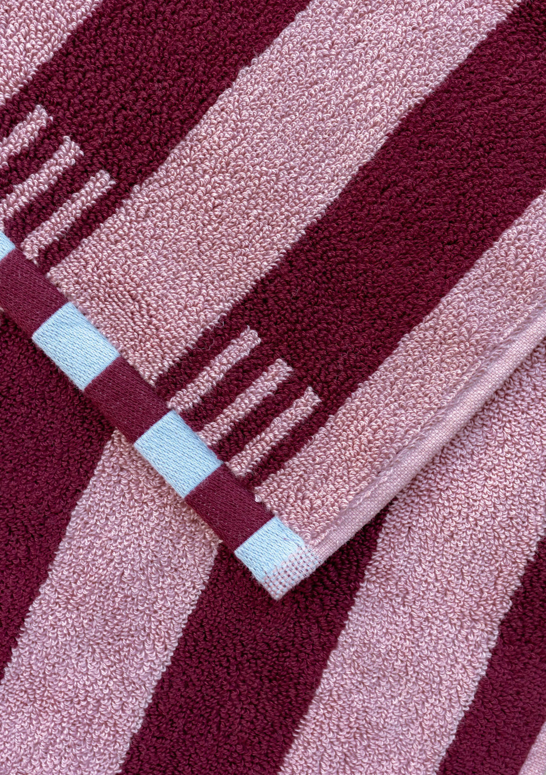 Close-up of TBCo Terry Cotton Towels in Burgundy Stripe showing plush cotton texture and blue checkerboard trim detail