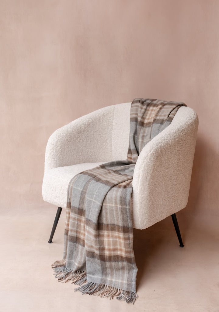 Cashmere Blanket in Mackellar Tartan by TBCo draped over a modern cream armchair with fringed edges.