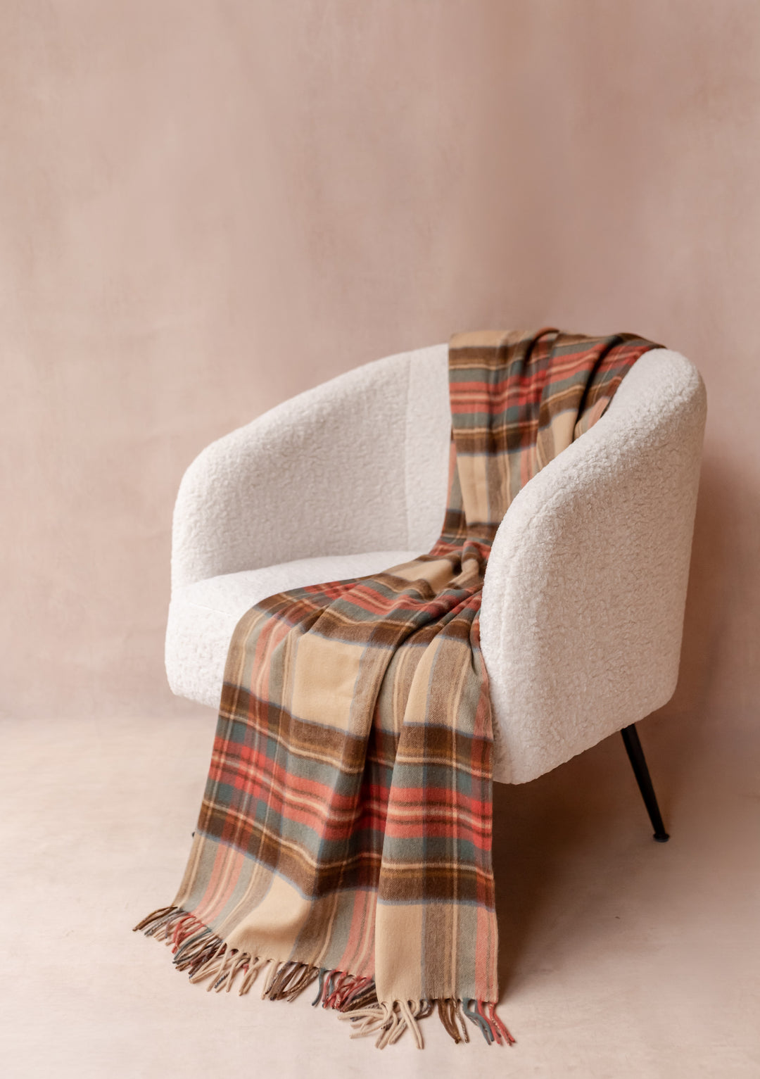 Cashmere Blanket in Stewart Dress Antique Tartan by TBCo draped over a cream boucle armchair with fringe detail.