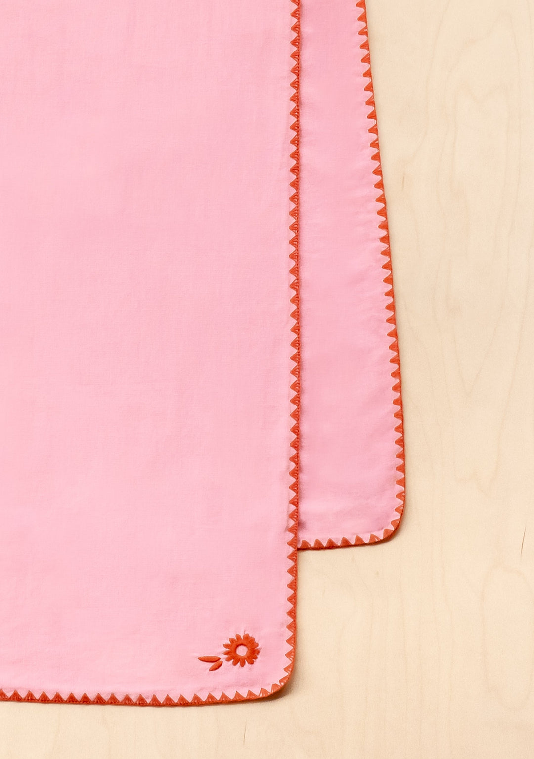 TBCo Cotton & Linen Table Runner in pink with orange embroidered edges and floral detail, photographed on beige surface
