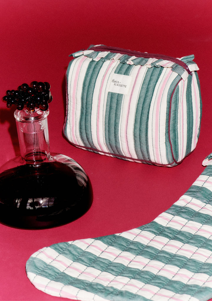 TBCo x Glassette Cotton Wash Bag in Green Stripe, featuring quilted texture, ruffle trim, and zip-top, with matching textile piece and decorative carafe nearby.