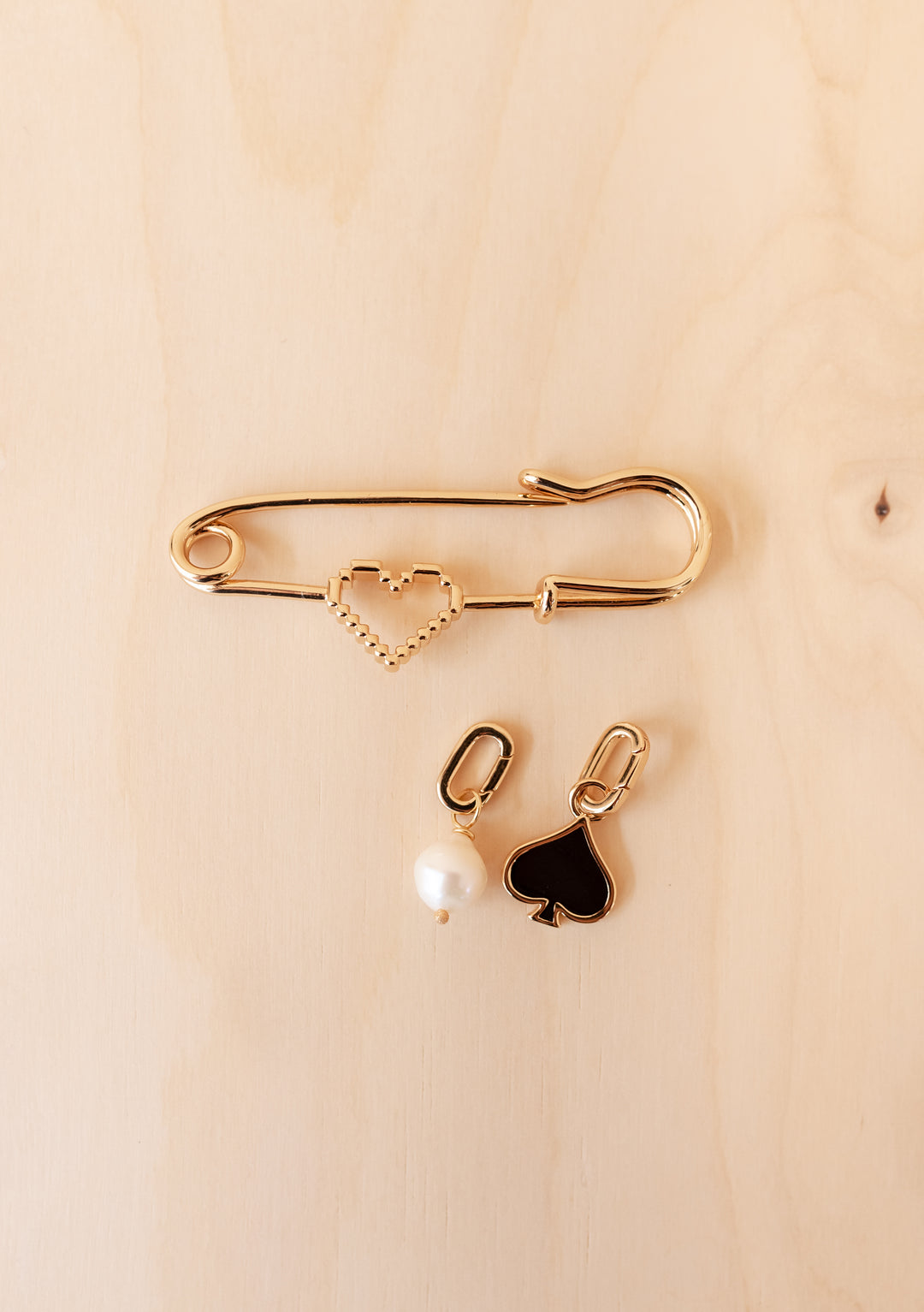 TBCo x frkl. Circus Scarf Pin: A gold-tone safety pin brooch with a pixelated heart and two charms—a pearl drop and a black spade.